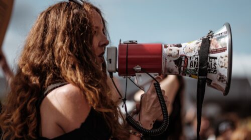 selective focus photography of woman wearing black cold-shoulder shirt using megaphone during daytime